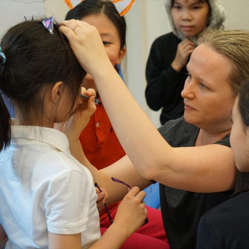 Female English drama teacher applying makeup on a Hong Kong student. Teacher and students preparing for a drama performance.