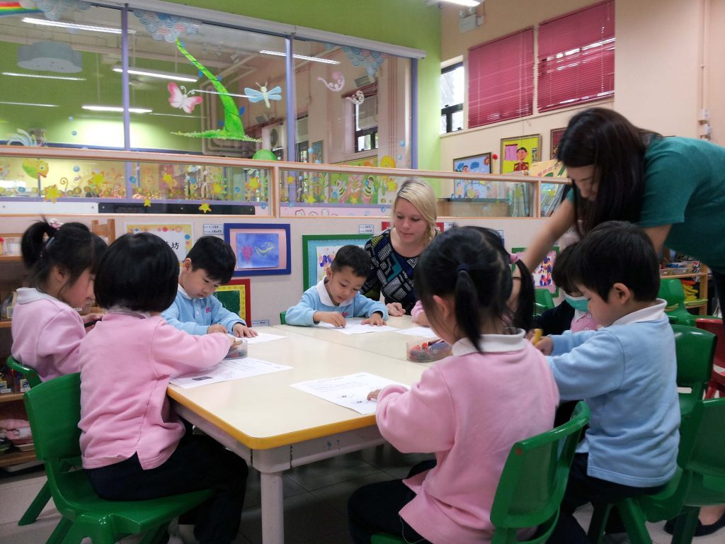 Female ESL teacher with kindergarten students doing worksheets.